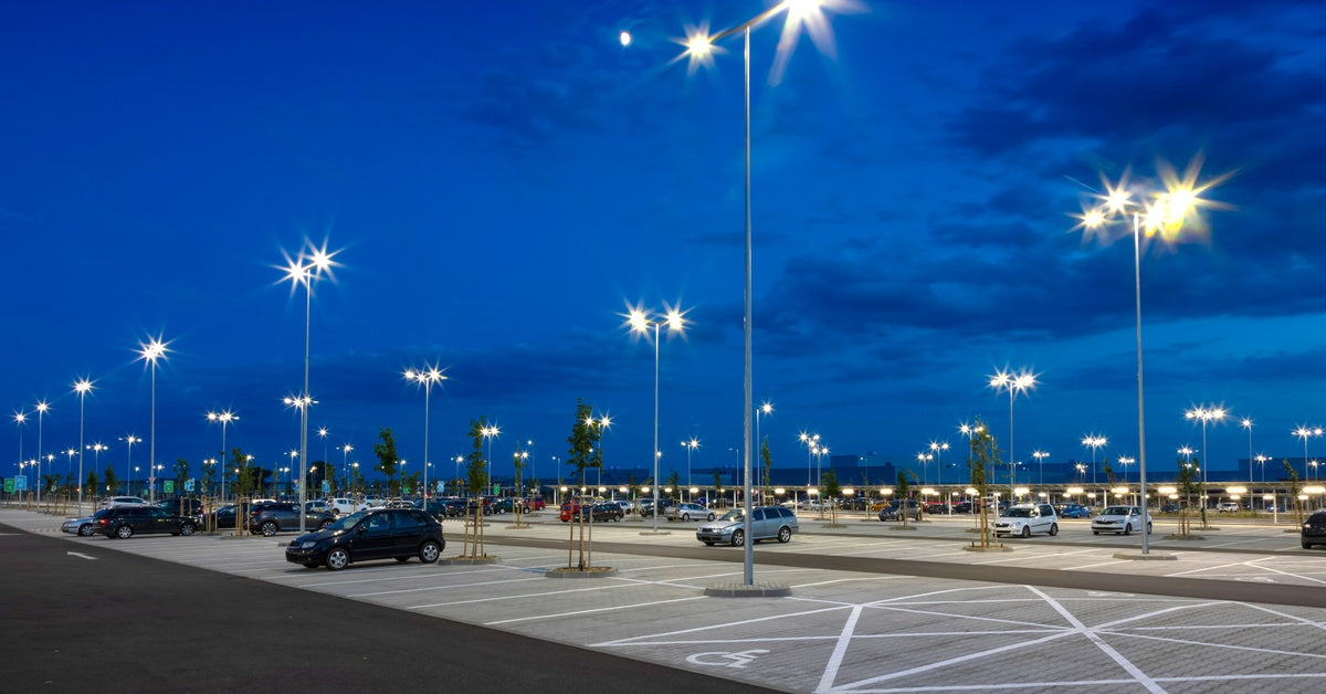 An expansive parking lot features sparse parked vehicles. Streetlamps are shining brightly against a dark blue sky.