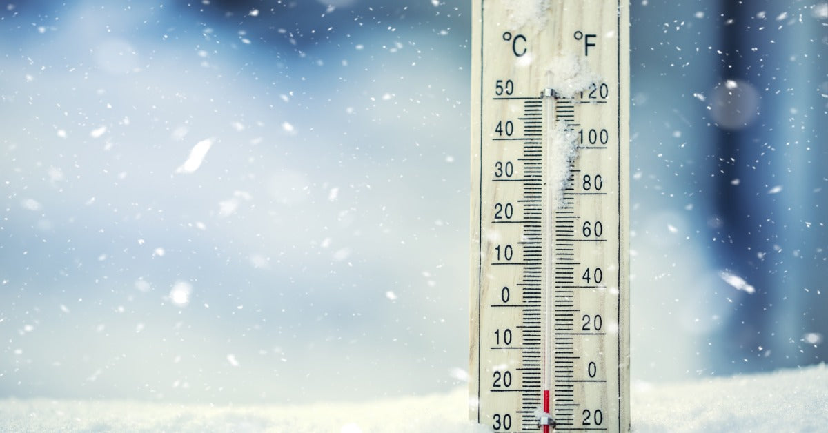 A thermometer sits in a pile of snow while flurries are in the air. Its temperature is below zero degrees Fahrenheit.