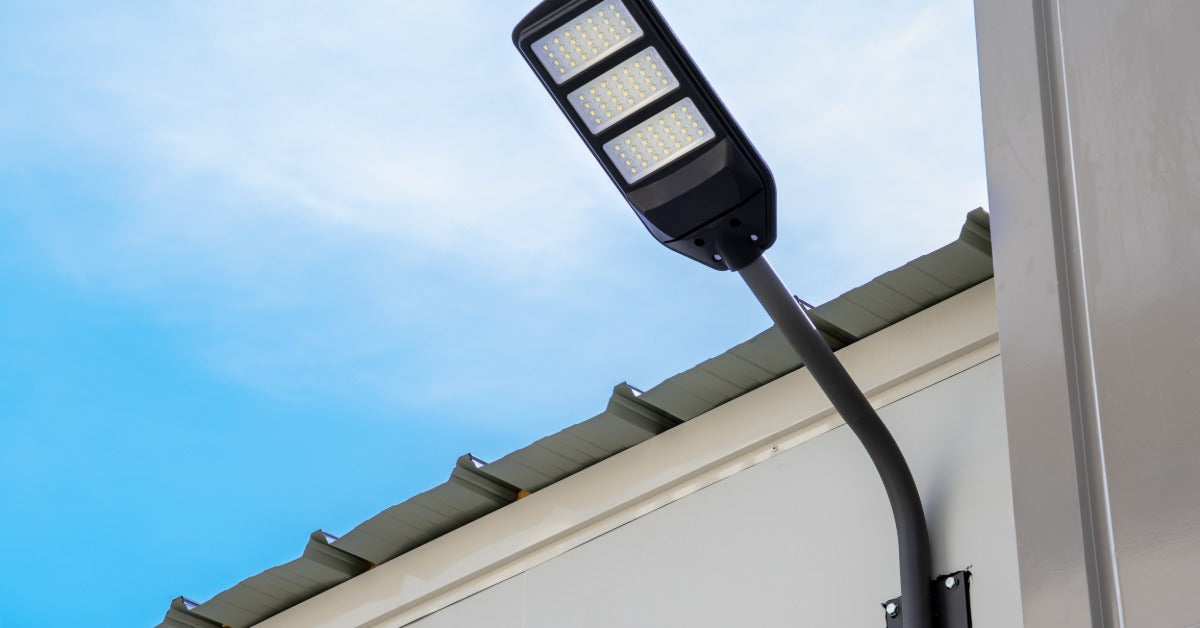 A wall-mounted solar light extends out from a building. In the background is a clear blue sky on a sunny day.