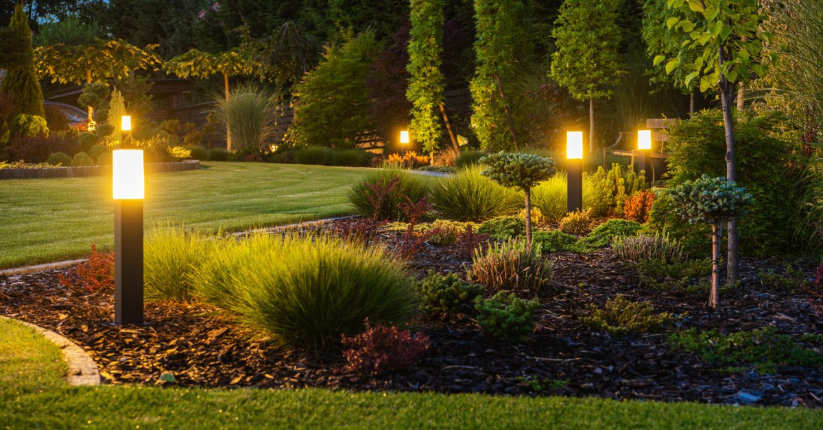 A large backyard with beautiful landscaping, including mulched pathways and small bushes. There are solar lights planted.