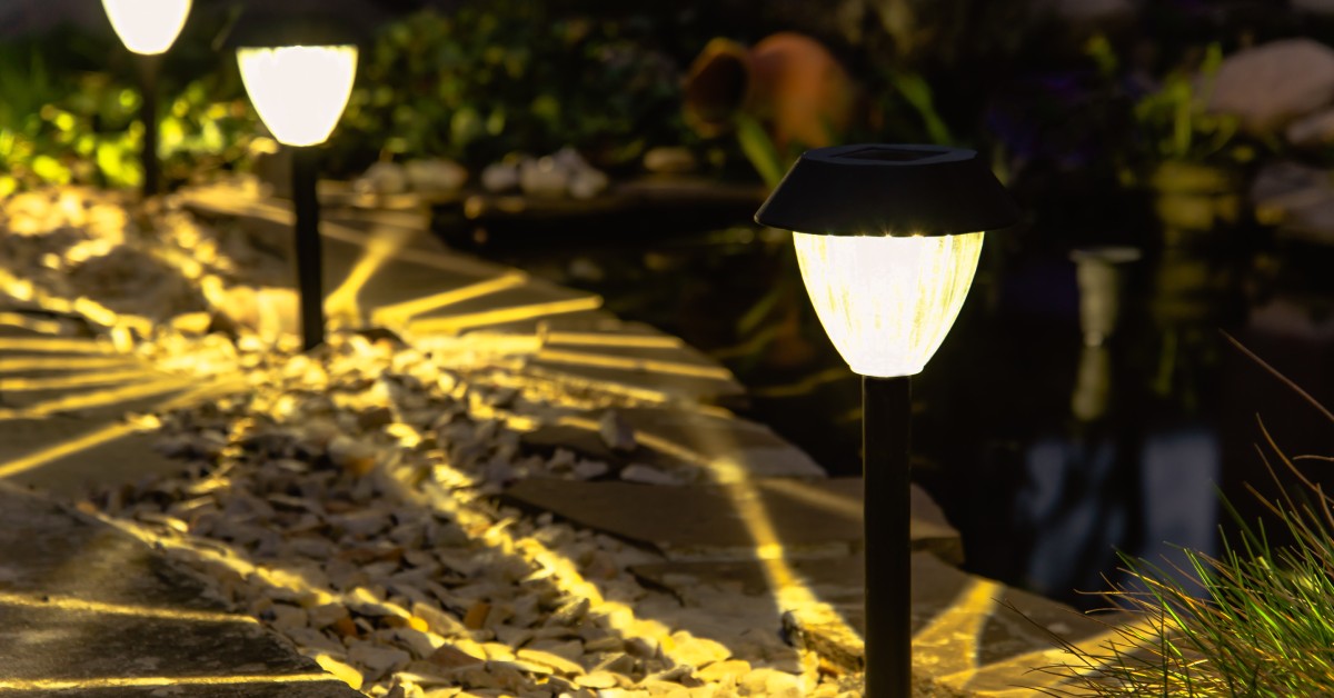 Solar lights shine along the edge of a garden at night. A pond sits on the garden's edge in the property.