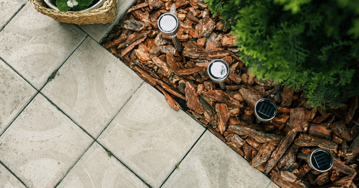 Overhead view of four solar lighting fixtures in a bed of mulch next to a tile patio and a basket of flowers.