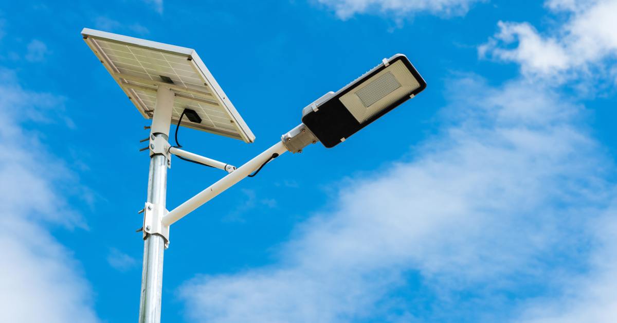 A solar street light stands up against a bright blue sky with white clouds. It has a solar panel at the top.