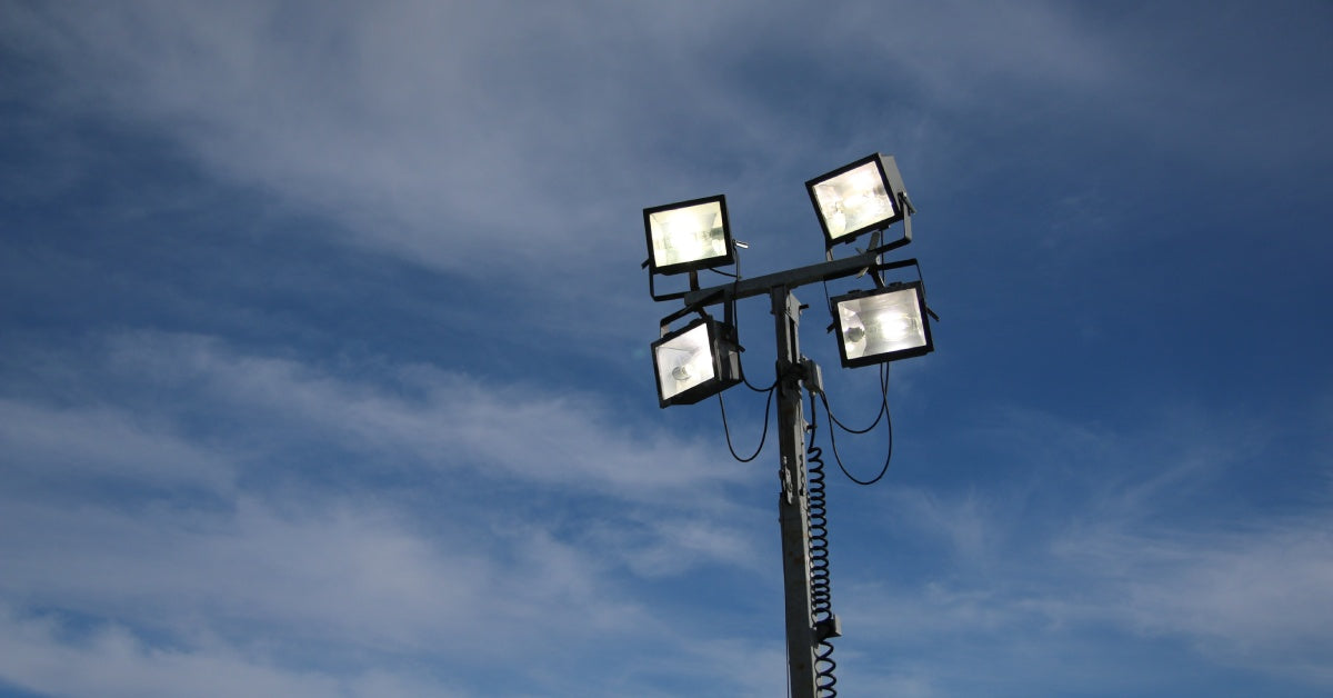 A portable lighting tower shines brightly in the air, in front of a sky filled entirely with gray clouds.
